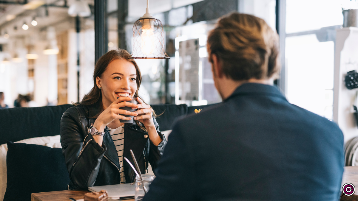 Couple smiling and talking over coffee on a first date at a restaurant.